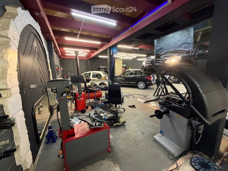 A well-lit garage with multiple cars, a hydraulic lift, a tire machine, and various tools and equipment.