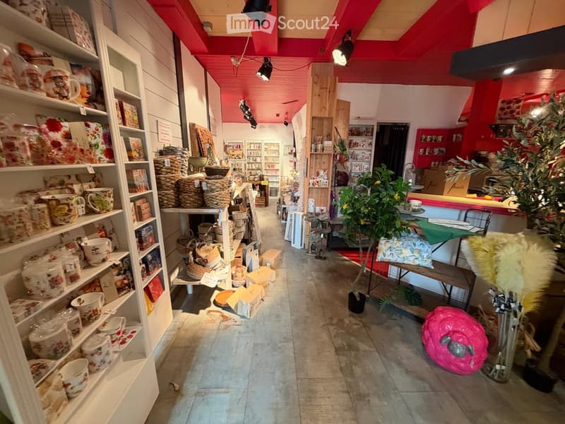 A well-lit store interior with red and white decor, featuring shelves filled with ceramic items, baskets, and decorative pieces, along with a small seating area and plants.
