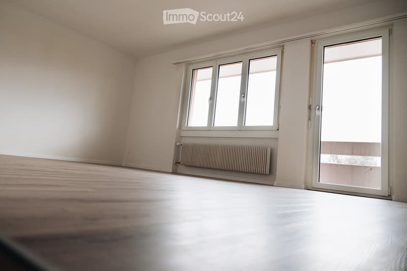 Empty room with light-colored walls, wooden floor, large windows, and a radiator. No furniture or equipment present.