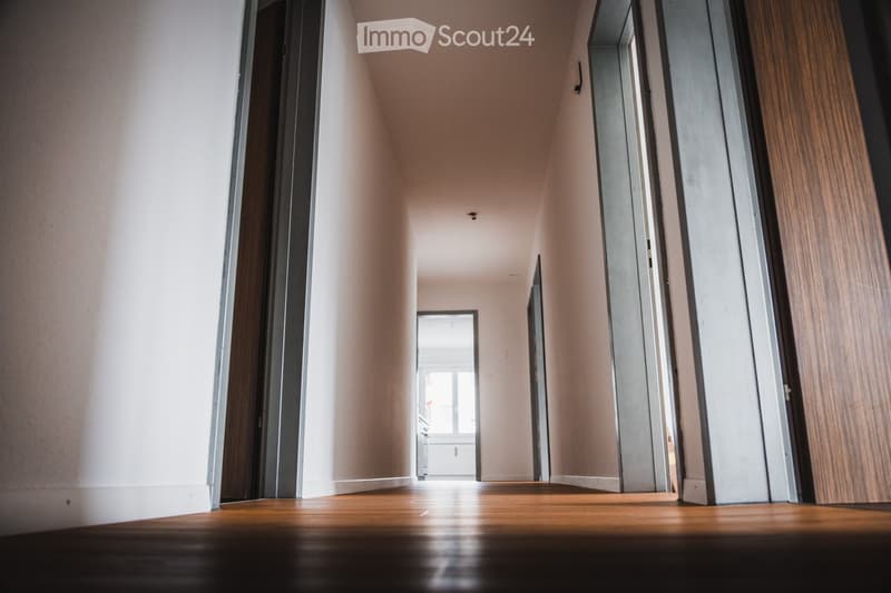 Empty hallway with wooden flooring, light-colored walls, and several doors leading to other rooms.