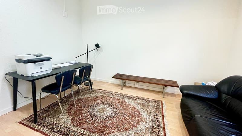 A furnished room with a black sofa, a wooden bench, a desk with a printer, two chairs, and a floor lamp.