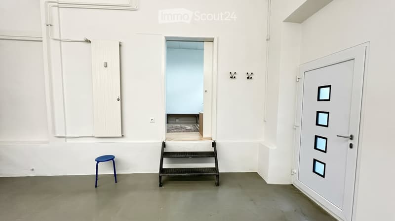 Empty room with white walls, grey floor, a small blue stool, a metal step ladder, and a closed door with square panels.