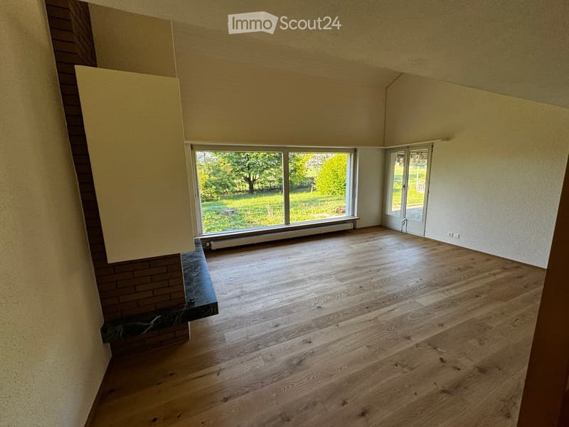 Empty room with wooden flooring, large windows, and a brick fireplace. No furniture or equipment present.