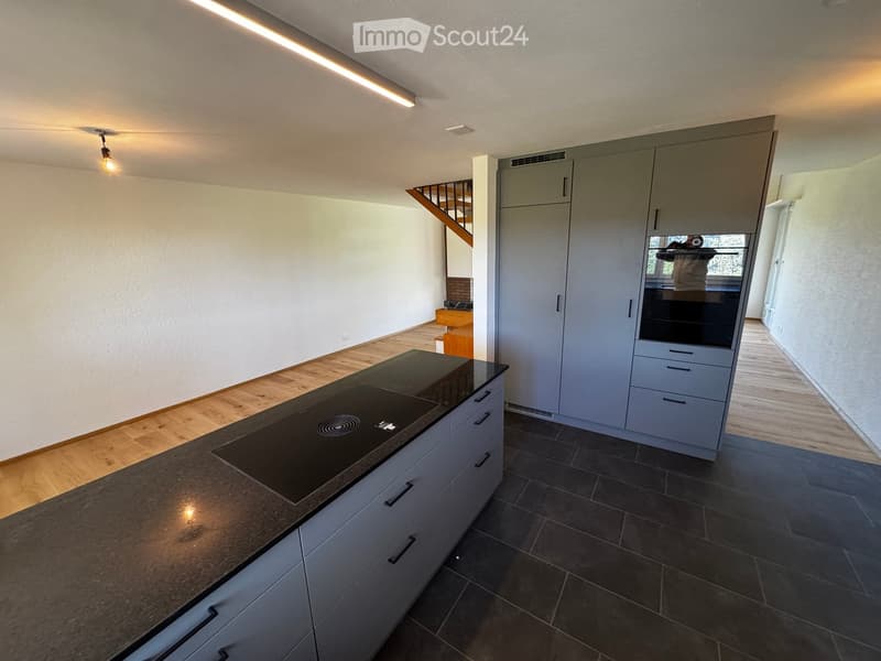 Modern kitchen with grey cabinets, a black kitchen island with an induction cooktop, and dark tiled flooring.