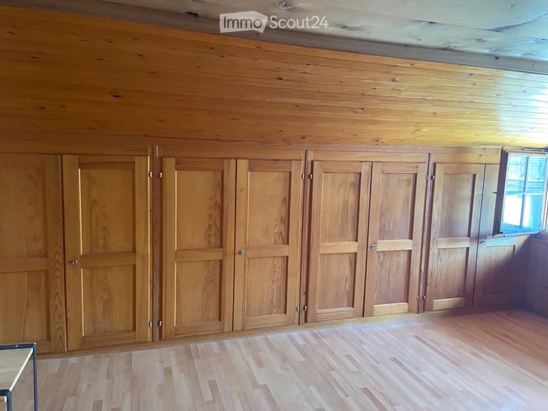 Empty room with wooden walls, wooden floor, and built-in wooden cabinets along one wall. A small window is visible on the right side.