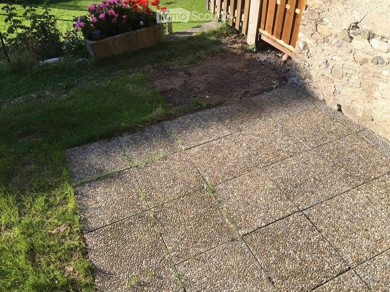 Gravel pathway leading to a wooden fence, with a small garden bed containing pink and red flowers on the left side.