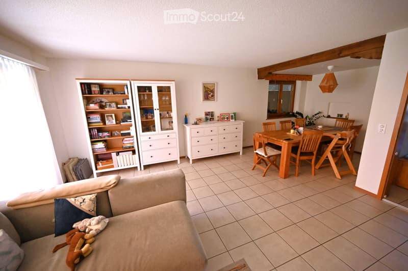 Living and dining area with a beige sofa, bookshelf, dining table, chairs, and decorative items.