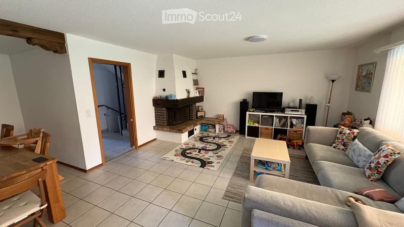 Living room with a sofa, coffee table, dining table, chairs, television, bookshelf, and toys.