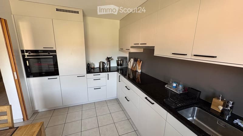 Modern kitchen with white cabinets, black countertops, and stainless steel appliances including an oven, sink, and faucet. Various kitchen items such as a blender, knife block, and cups are visible on the countertops.