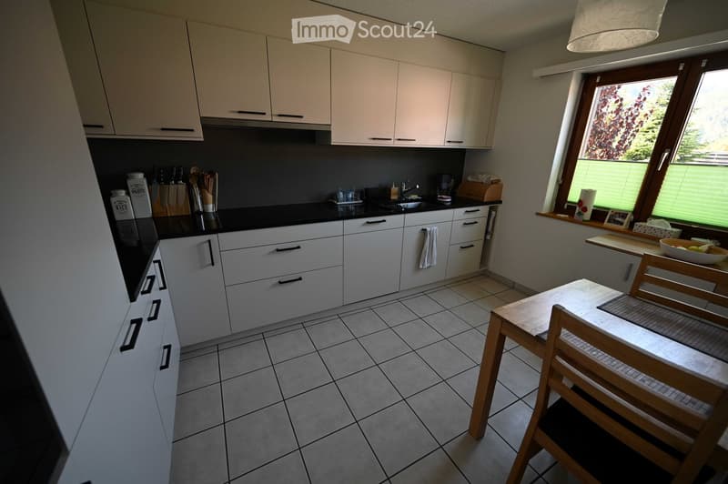 Modern kitchen with white cabinets, black countertops, tiled floor, and a small dining area with a table and chairs.
