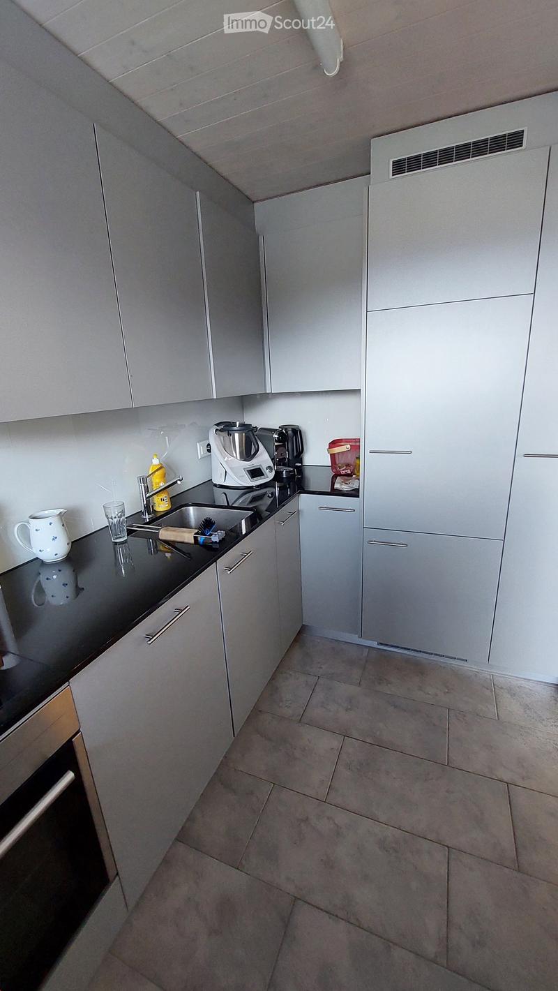 Modern kitchen with grey cabinets, black countertop, sink, coffee maker, cup, teapot, and bottle on the counter.