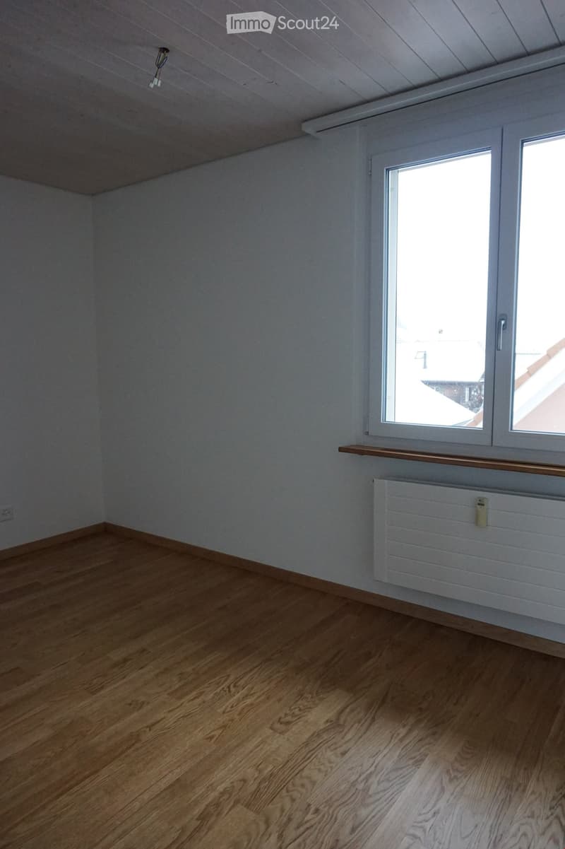 Empty room with wooden flooring, white walls, and a window with a wooden sill. A radiator is visible below the window.