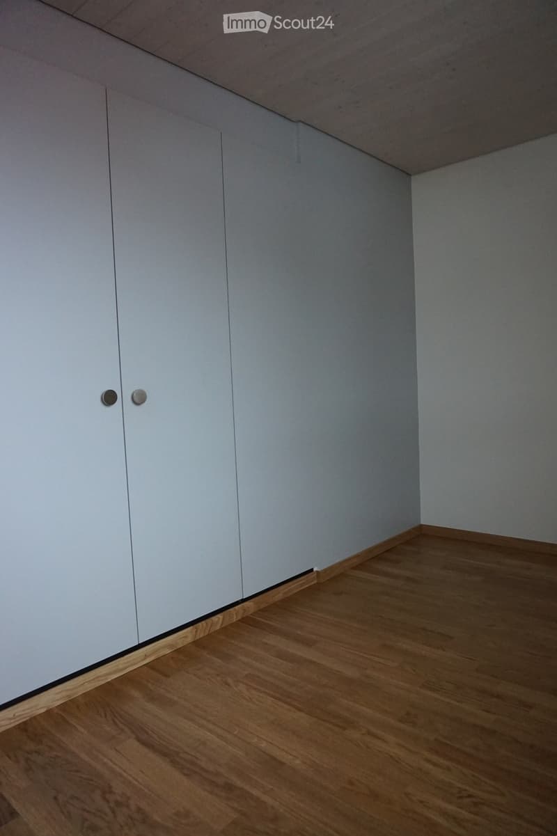 Empty room with light grey walls and wooden flooring, featuring a set of white built-in cabinets on one side.
