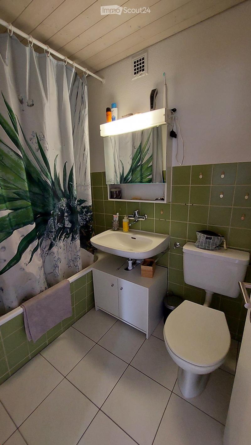 Bathroom with green tiled walls, white sink, toilet, mirror, and a shower curtain with a leafy design.