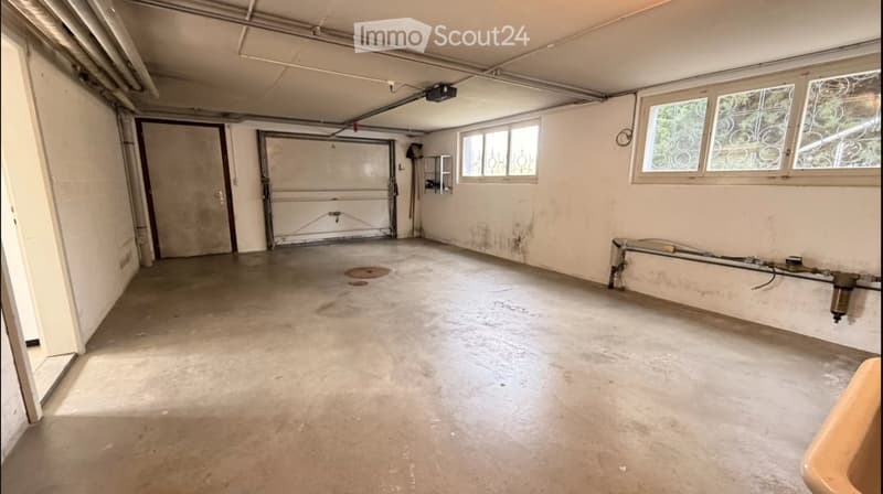 Empty garage with concrete floor, white walls, large garage door, and windows with decorative glass.