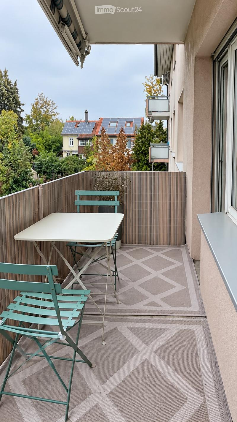 Balcony with a small table and two chairs, wooden railing, and a potted plant.
