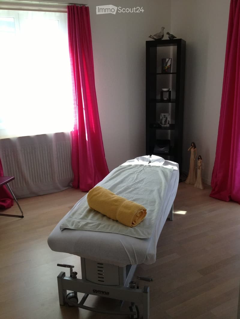 A well-lit room with a massage table, a shelf with decorative items, and two statues near the window.