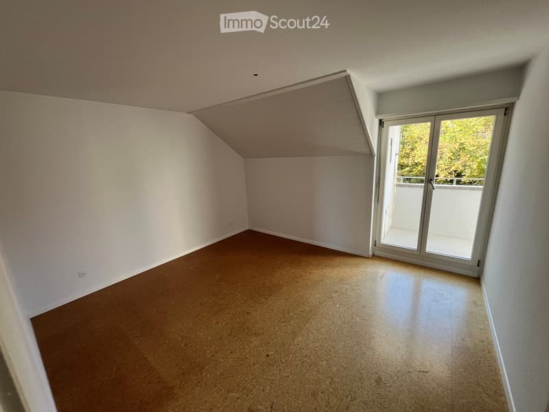 Empty room with light-colored walls, wooden floor, and large sliding glass door leading to a balcony.