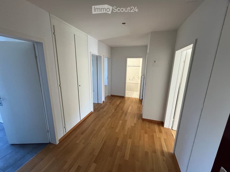 Empty hallway with wooden flooring, white walls, and multiple doors leading to other rooms.
