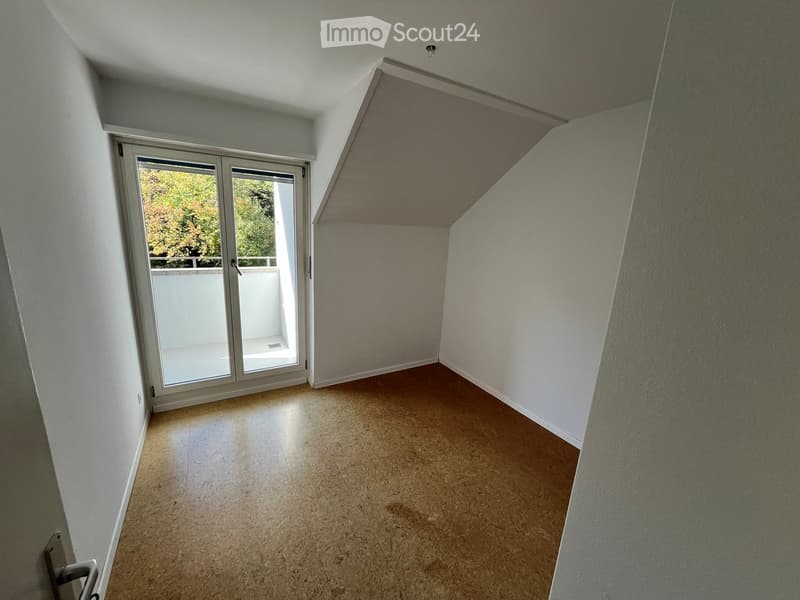 Empty room with slanted ceiling, tiled floor, and sliding glass door leading to a balcony.