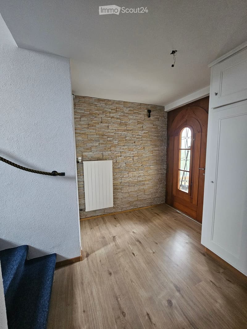 Empty room with wooden flooring, white walls, stone accent wall, white radiator, and a wooden door with glass panel.