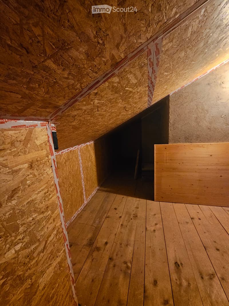 Empty attic space with exposed wooden beams, insulation, and a wooden floor. No furniture or equipment present.