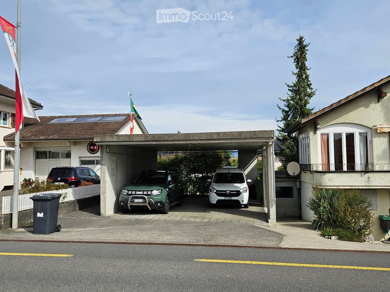 Two-story house with a covered garage containing three parked cars, solar panels on the roof, and a small garden area.