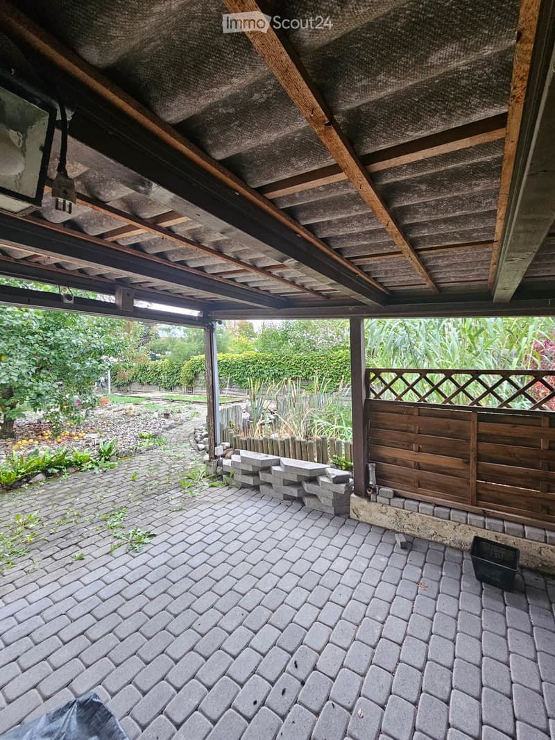 Outdoor patio with brick pavement, wooden fence, and visible garden area with plants and trees.