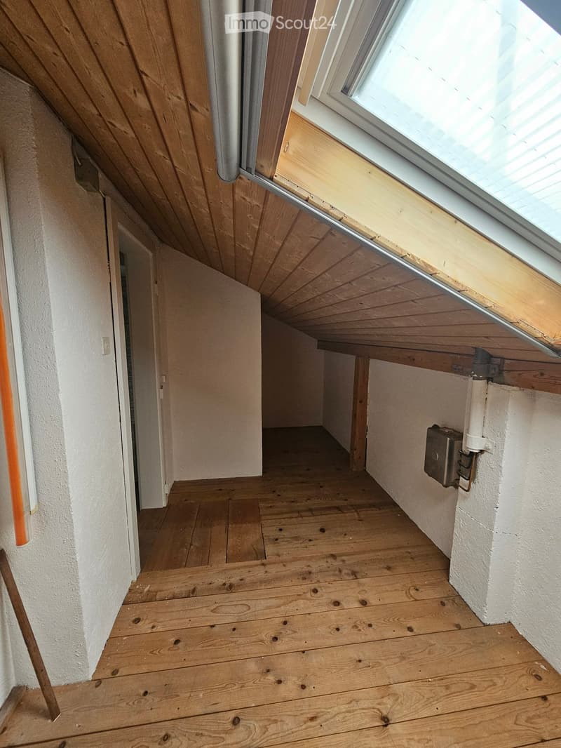 Empty wooden-floored hallway with white walls, a partially open door, and a skylight window at the far end.