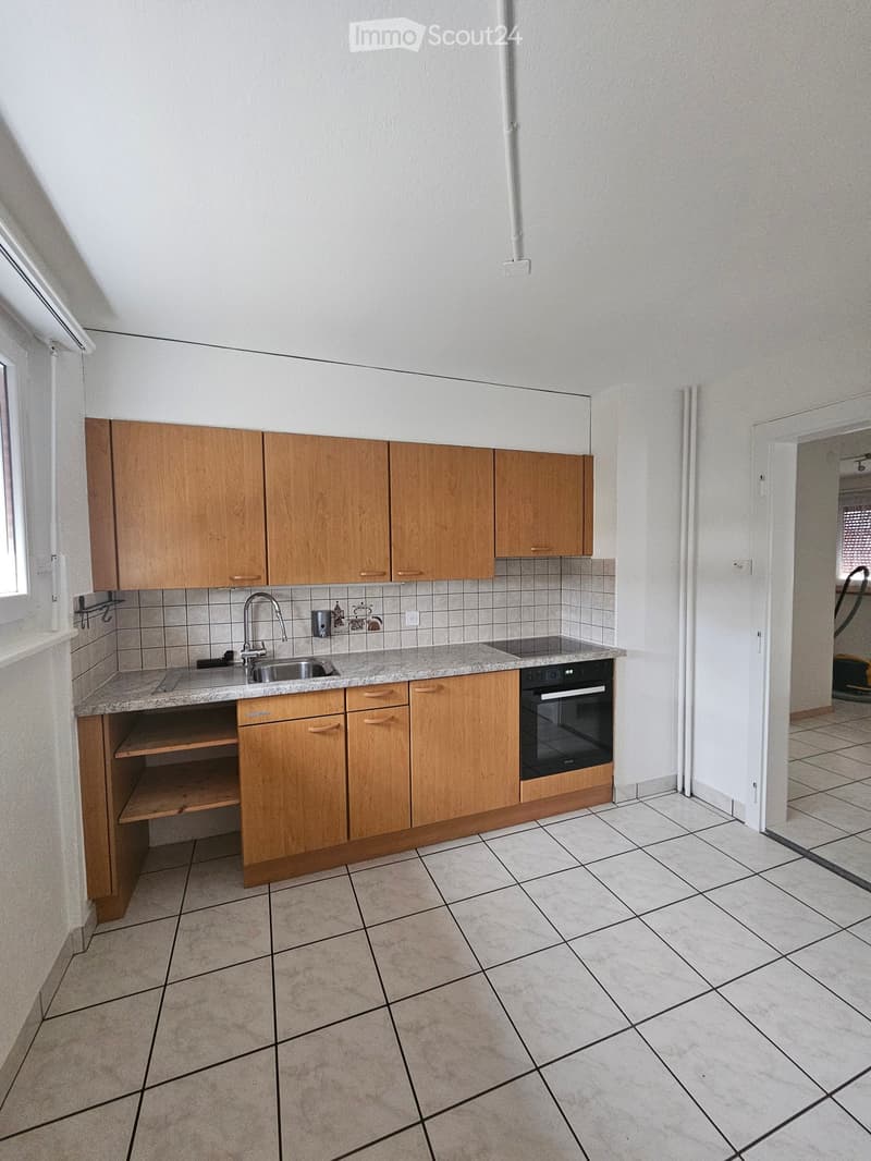 Empty kitchen with wooden cabinets, tiled walls, and a granite countertop. Includes a sink, faucet, and built-in oven.