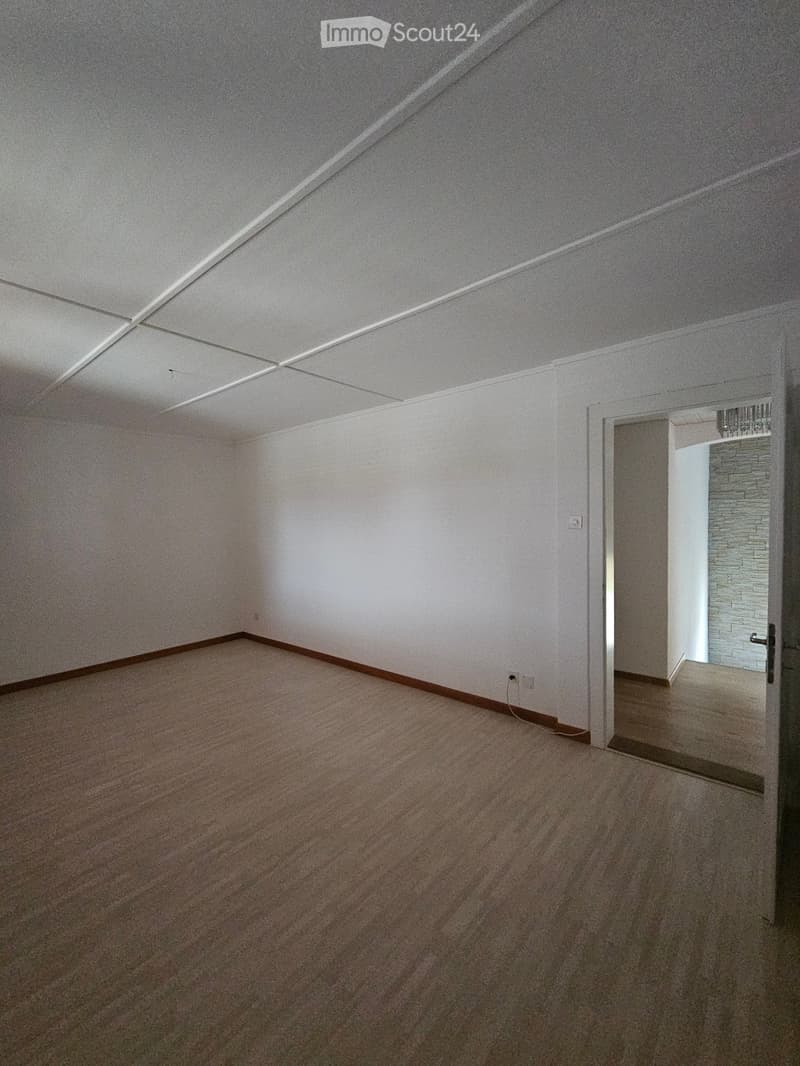 Empty room with white walls, carpeted floor, and a door leading to another space.