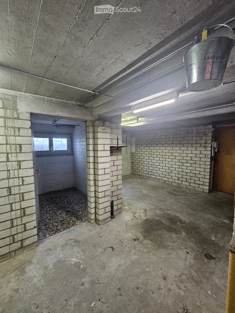 Empty underground garage with concrete floors, brick walls, and a small windowed door leading outside.