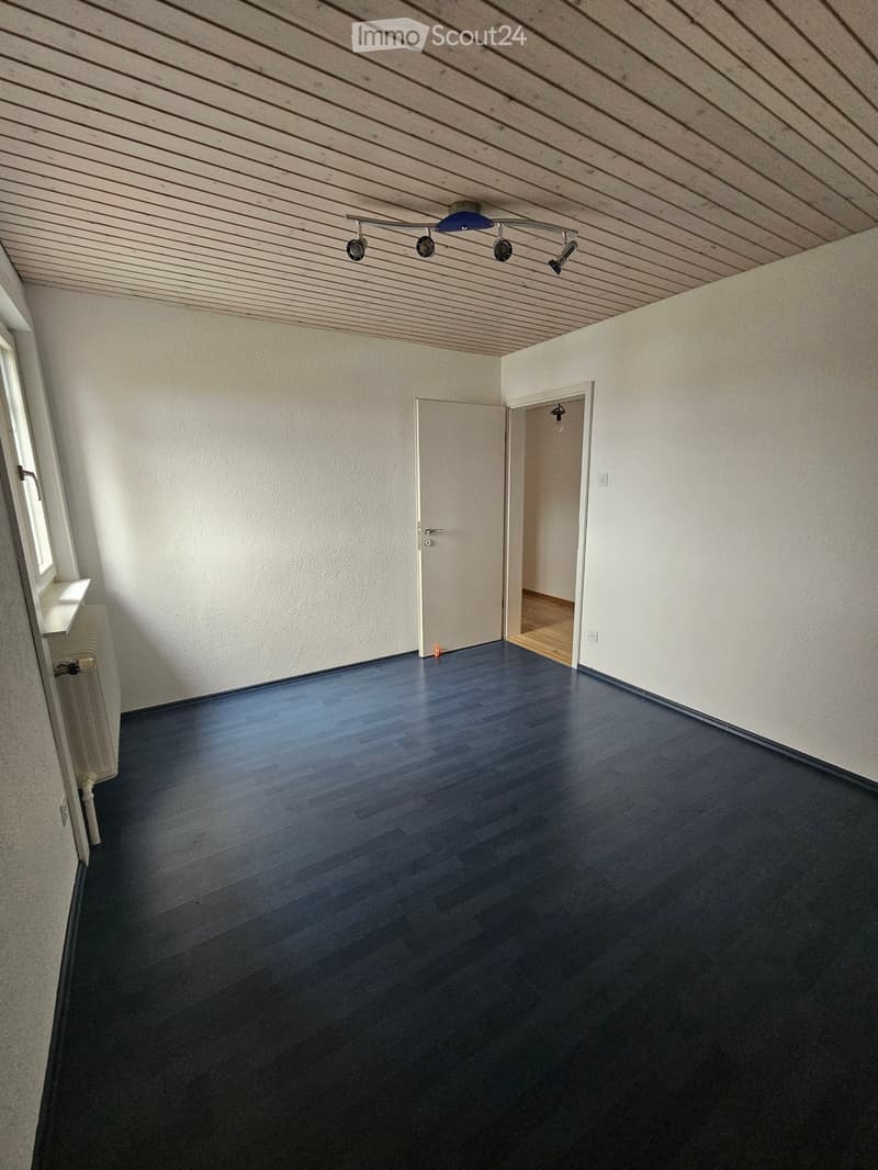 Empty room with dark wooden flooring, white walls, and a wooden ceiling with track lighting. Two doors are visible, one leading to another room.
