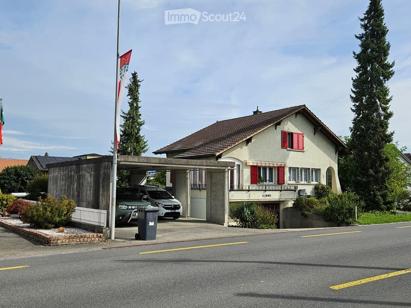 Two-story house with a tiled roof, red shutters, and a covered driveway with two parked cars.