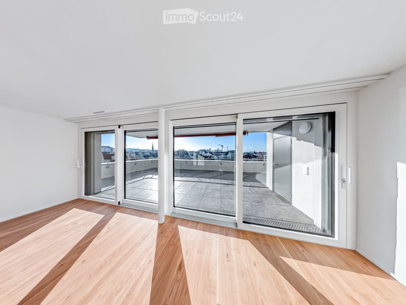 Empty room with wooden flooring, white walls, and large sliding glass doors leading to a balcony with a city view.