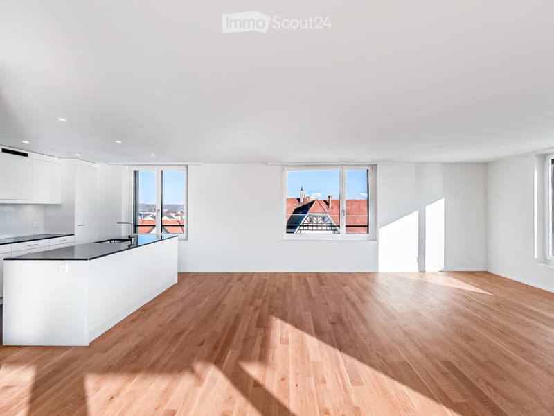 Modern kitchen with white cabinets, a central island, wooden flooring, and large windows offering a city view.