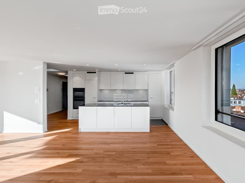Modern kitchen with white cabinets, a central island, and a large window offering a view. The space features light wooden flooring and ample natural light.