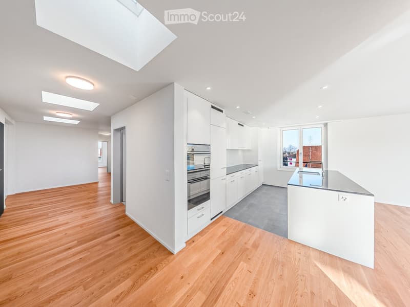 Modern kitchen with white cabinets, stainless steel appliances, and a central island with a sink and faucet. The space features wooden flooring and large windows allowing natural light.