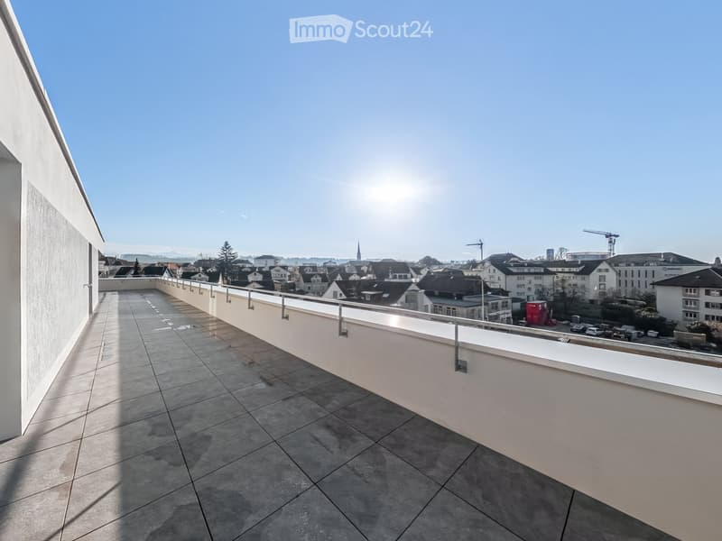 Modern balcony with tiled floor, white railing, and a view of a cityscape with buildings and construction cranes.