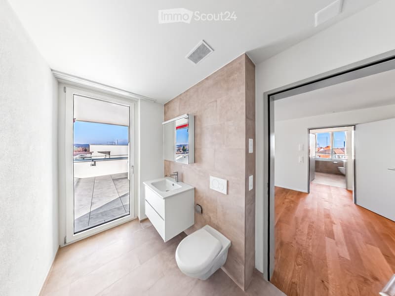 Modern bathroom with white tiles, a floating sink, toilet, and mirrored cabinet. Large window offers a view of the balcony and outdoor area.