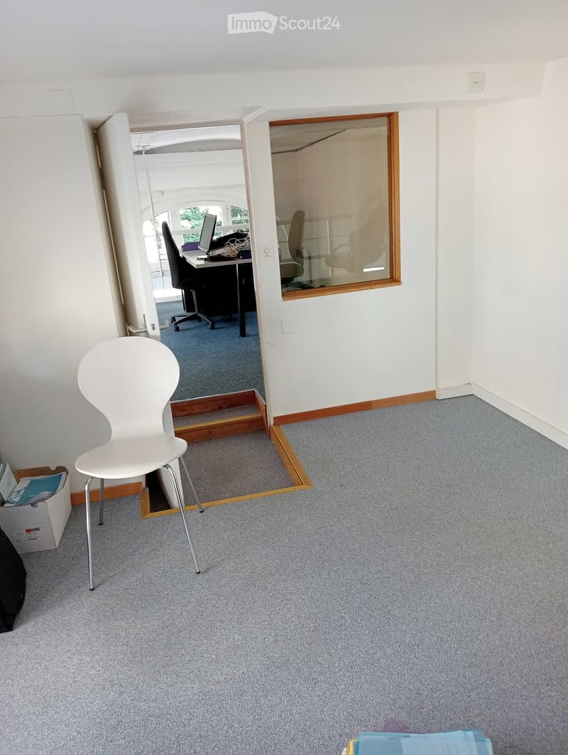A furnished room with a white chair, a desk with a computer, and an office chair visible through an open doorway.