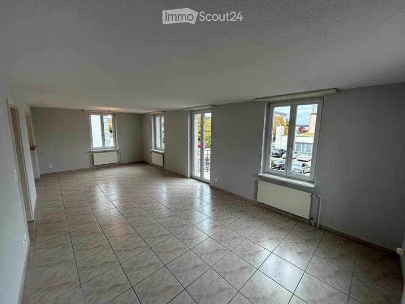 Empty room with tiled floor, grey walls, multiple windows, radiators, and a sliding glass door leading to an outdoor area.