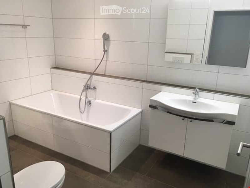 Modern bathroom with white tiles, a bathtub, a sink with a cabinet, and a mirror above it.
