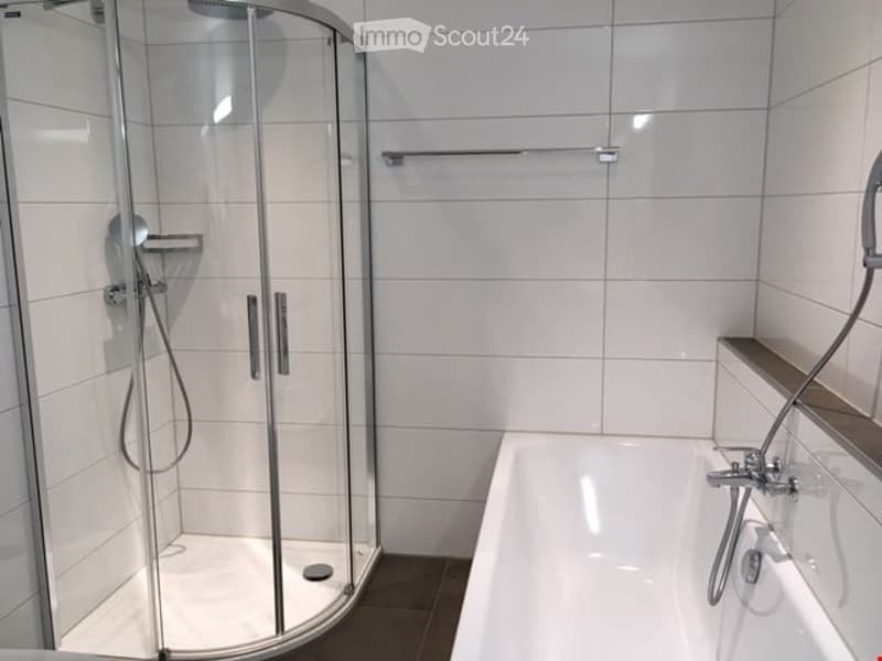 Modern bathroom with a white bathtub, a glass-enclosed shower stall, and a towel rack on the wall.