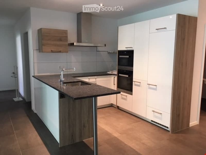 Modern kitchen with white cabinets, wooden accents, a central island with a sink, and built-in ovens.