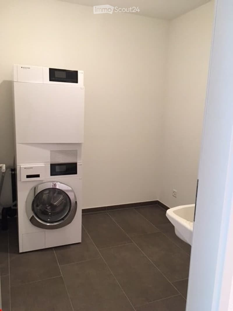 Bathroom with a washing machine and a bathtub, tiled floor, white walls.