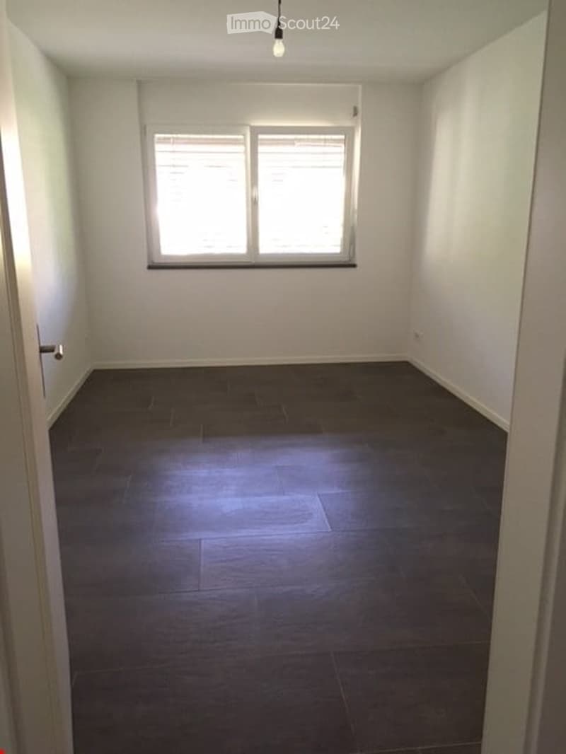Empty room with dark tiled floor and white walls, featuring a large window with blinds and a single ceiling light fixture.