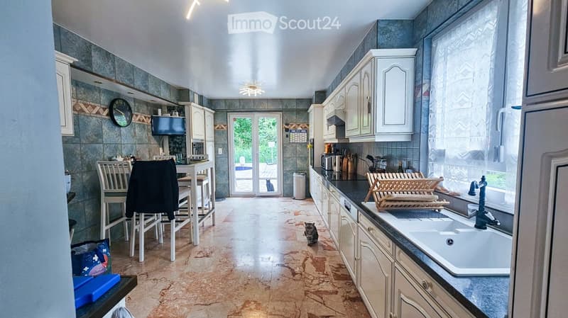 Bright kitchen with white cabinets, a central island, and a dining area. Features include a sink with a modern faucet, a clock on the wall, and a cat in the center of the room.