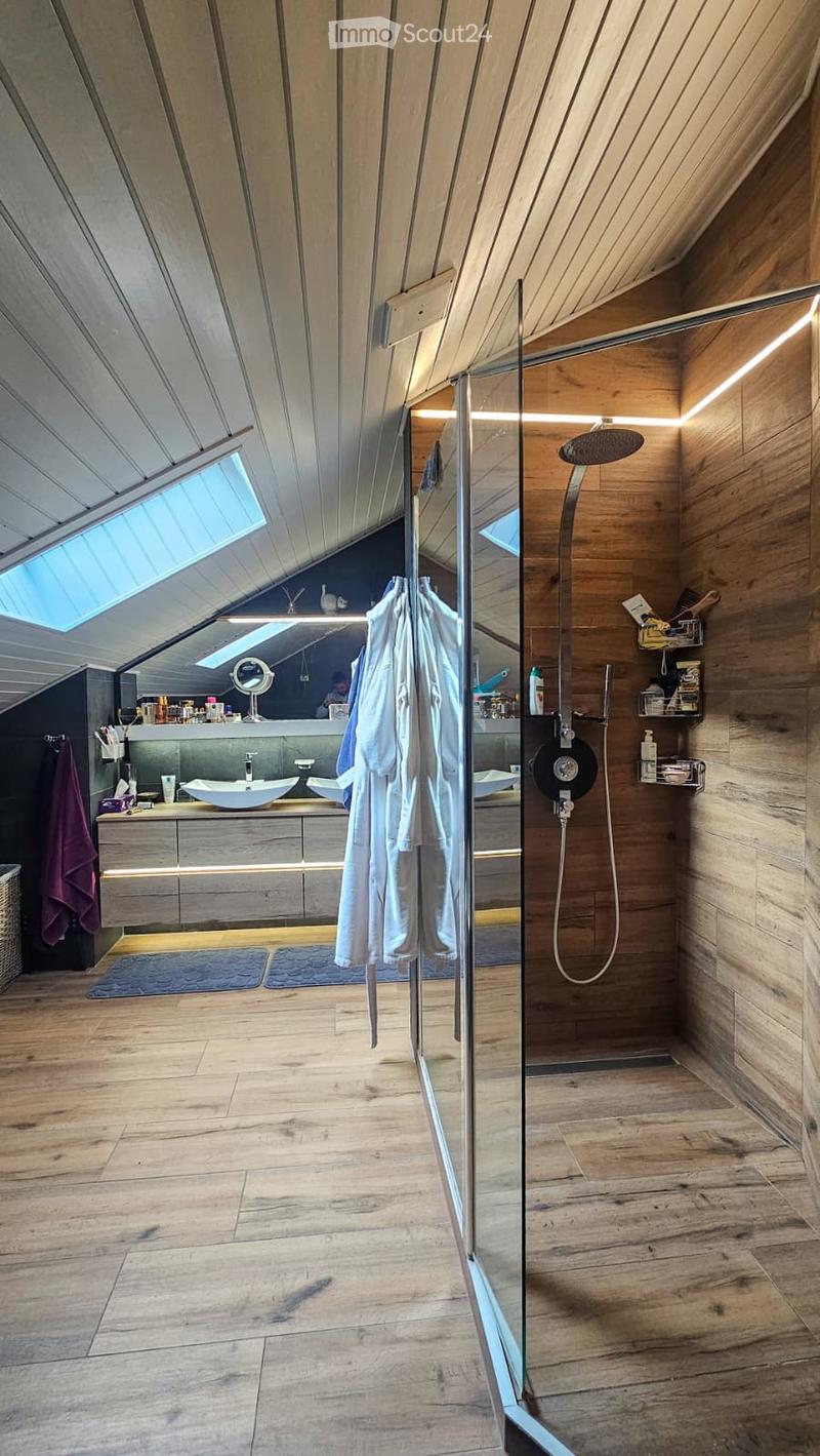 Modern bathroom with wooden walls and floor, featuring a large glass-enclosed shower, double sink vanity, and built-in storage shelves.