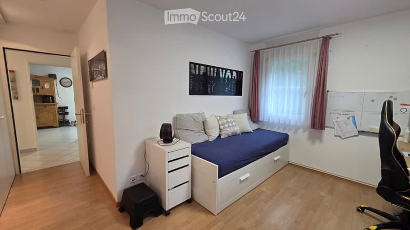 Cozy bedroom with a single bed, nightstand, chair, and a small cabinet visible in the adjacent room.